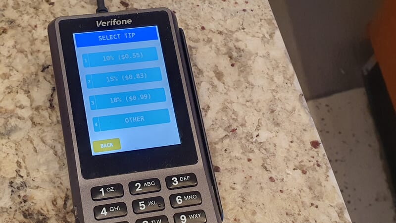 Photograph of a card payment terminal showing three percentage tipping options (10, 15, 18%), an 'other' option, but no option not to tip