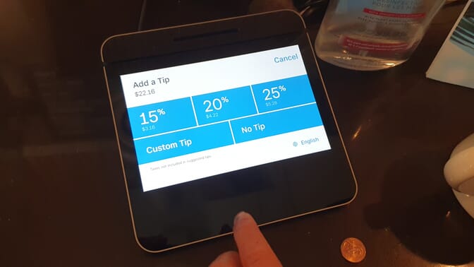 Photograph of a card payment terminal showing three percentage tipping options (15, 20, 25%), a custom tip option, and a no tip option